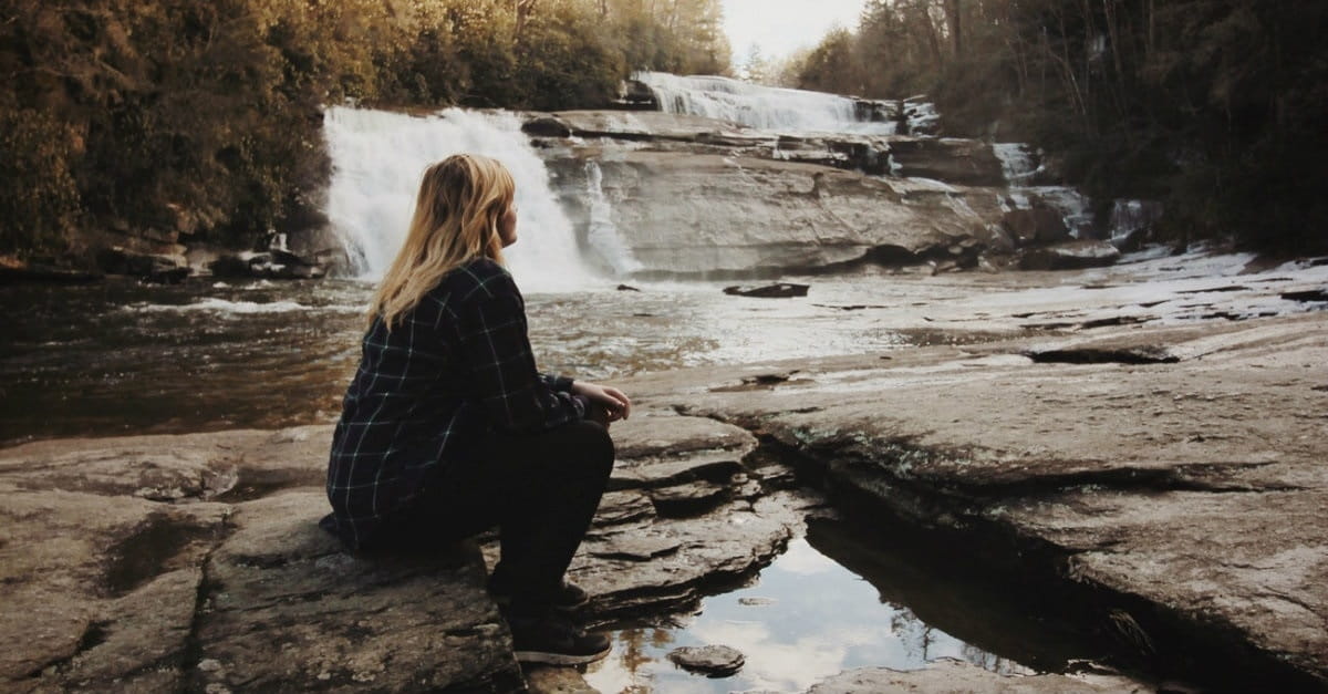 Woman sitting by a waterfall, looking into the distance