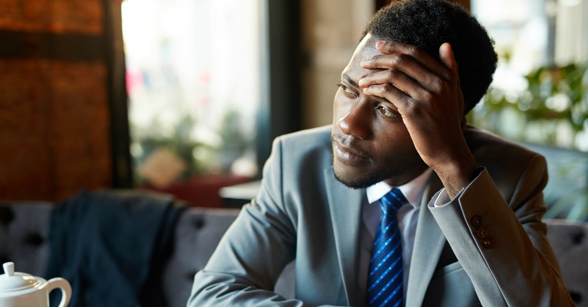 businessman in suite holding forehead and looking wistfully off toward windows in cafe