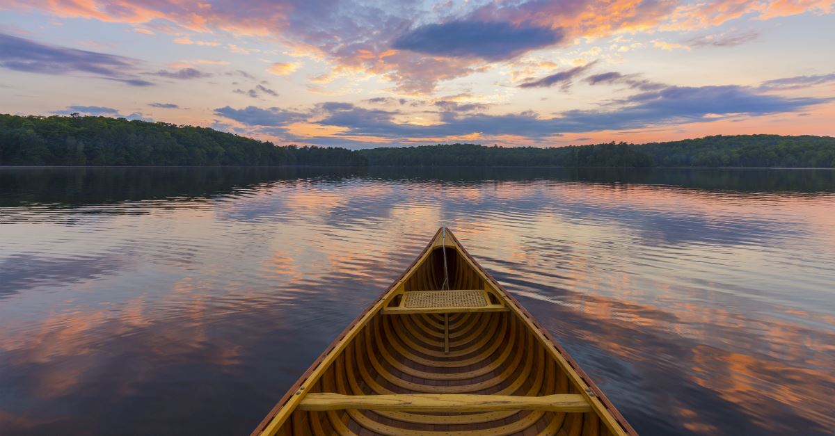 bow of cedar canoe heading along water at sunset