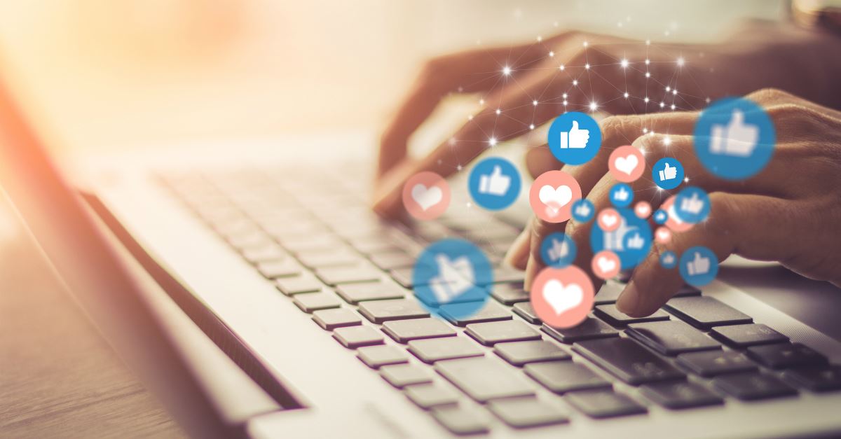 closeup of hands typing away on laptop with social media icons floating up from keyboard