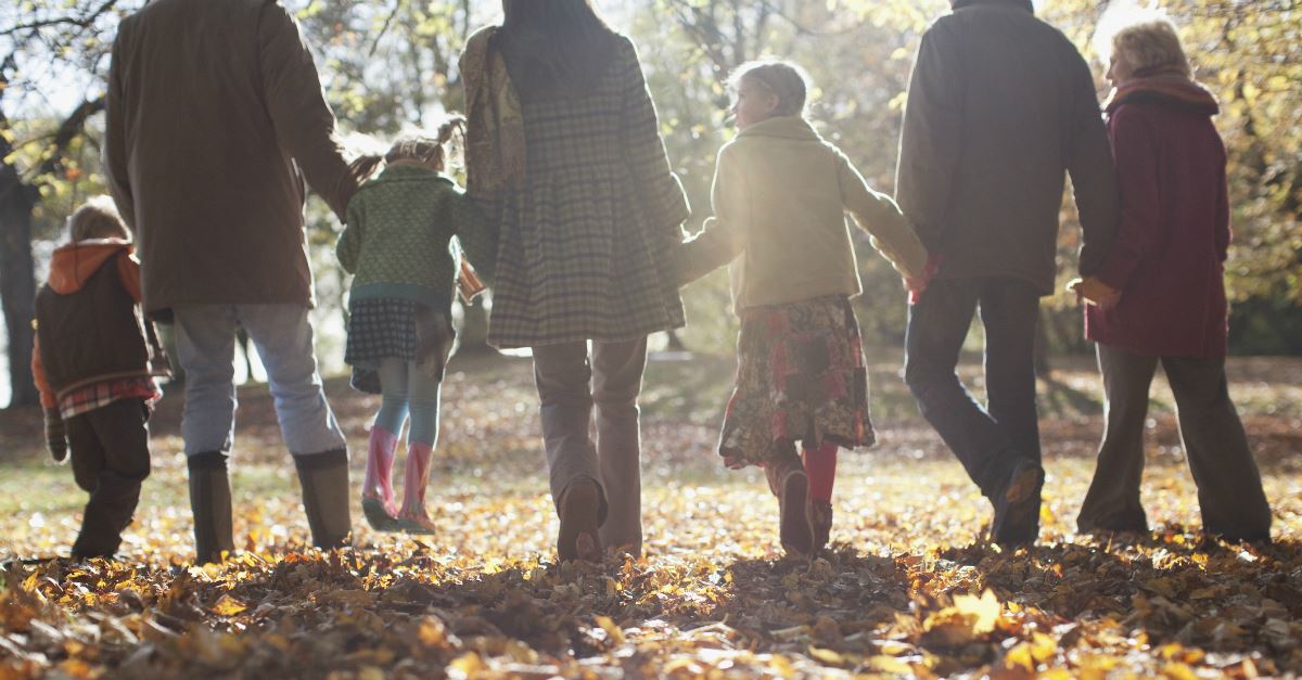 back view of extended family walking through fall leaves