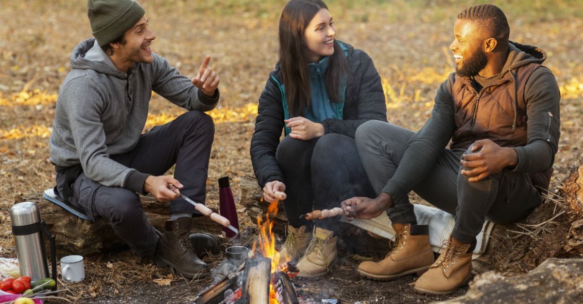 adult friends enjoying roasting hot dogs over a campfire