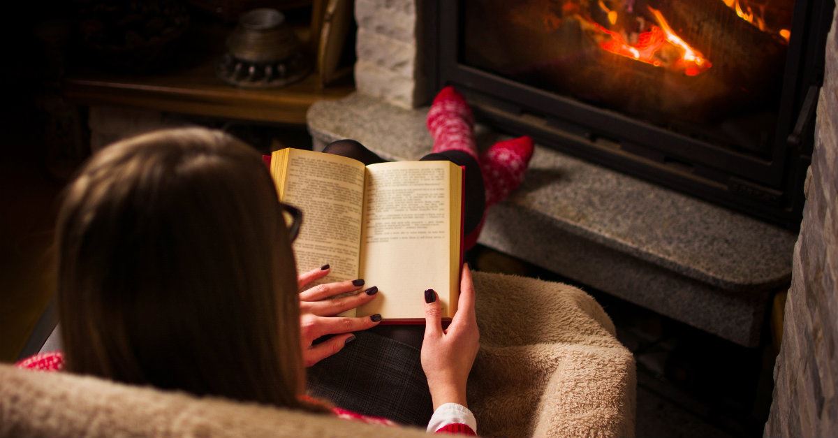 girl reading a book by the fireplace