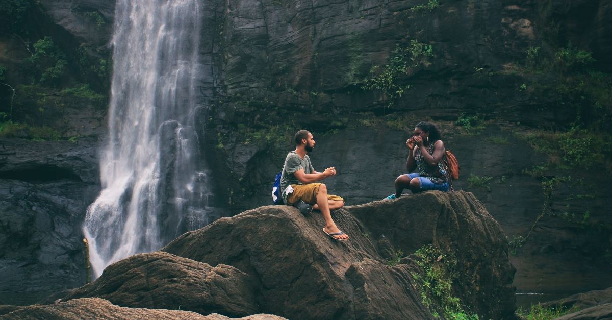 couple sitting on rock by waterfall