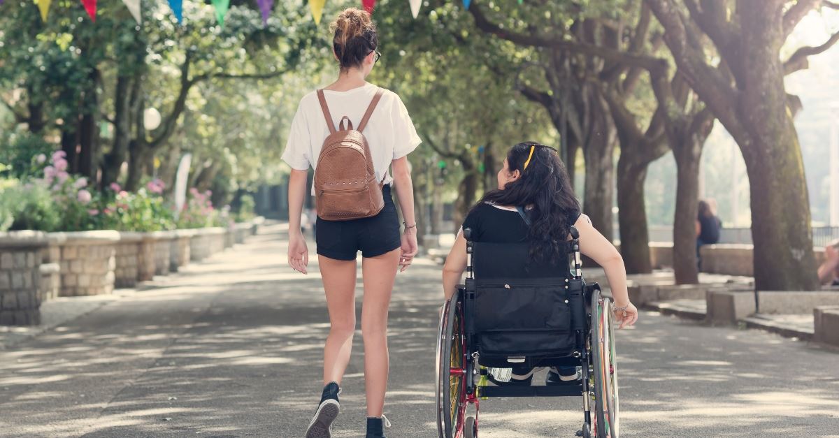 girls walking with wheelchair down park street