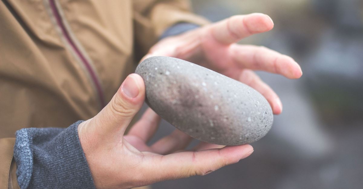 hands holding rock up close, lighten your load with a pile of stones