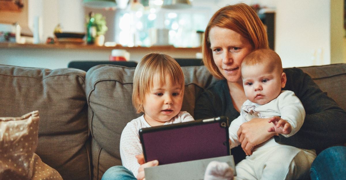 mom sitting with babies on couch with ipad