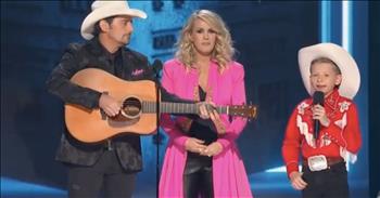 Kid Yodeler Mason Ramsey took the internet by storm when his performance of “Lovesick Blues” in the middle of a Walmart went viral. Taking the stage with Brad Paisley and Carrie Underwood at the CMA Awards, Mason Ramsey adorably posed as Carrie’s son and sang his heart out. Affectionately called “Little Hank” for his striking vocal resemblance to country great Hank Williams, Mason Ramsey is quickly rising as a household name.

As with any Awards show, the CMA’s insert deliberately hokey scripts between sets. In this silly segway, Paisley jokingly announces that “Carrie’s first born son” is coming out to perform for the audience. Cue kid yodeler, Mason Ramsey dolled up in his traditional Hank Williams styled western shirt with tassels and 10-gallon hat. Singing a spoof about being a new big brother at Christmastime (no, he’s not Carrie’s son) to the tune of ‘Lovesick Blues’, Mason easily stole the show!

“I’ve got the big brother blues, oh Lawdy, used to be an only child, and now I don’t know what to dooooo….And all those presents underneath the tree, now they ain’t all for me!”

Playing along well with seasoned performers, Paisley and Underwood, “Lil’ Hank” kept up quite nicely. This kid definitely has a unique star power about him! Even famous child star Brenda Lee has something to say about Mason!

“Mason is very talented, and seems very comfortable with his new fame and loving what he does,” says Brenda Lee, one of the first-ever country music child stars who, like Mason, recorded Hank Williams’ “Jambalaya.” She too was 11 at the time, in 1956.

We hope to see more of the kid yodeler and that he continues loving music and singing out those classic country tunes we all know and love! 
