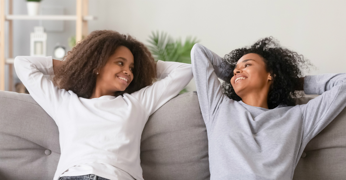 mom and teen daughter relaxing and smiling on couch hands behinds heads