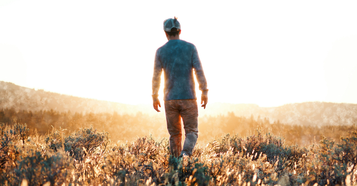 man walking through field toward sunlight