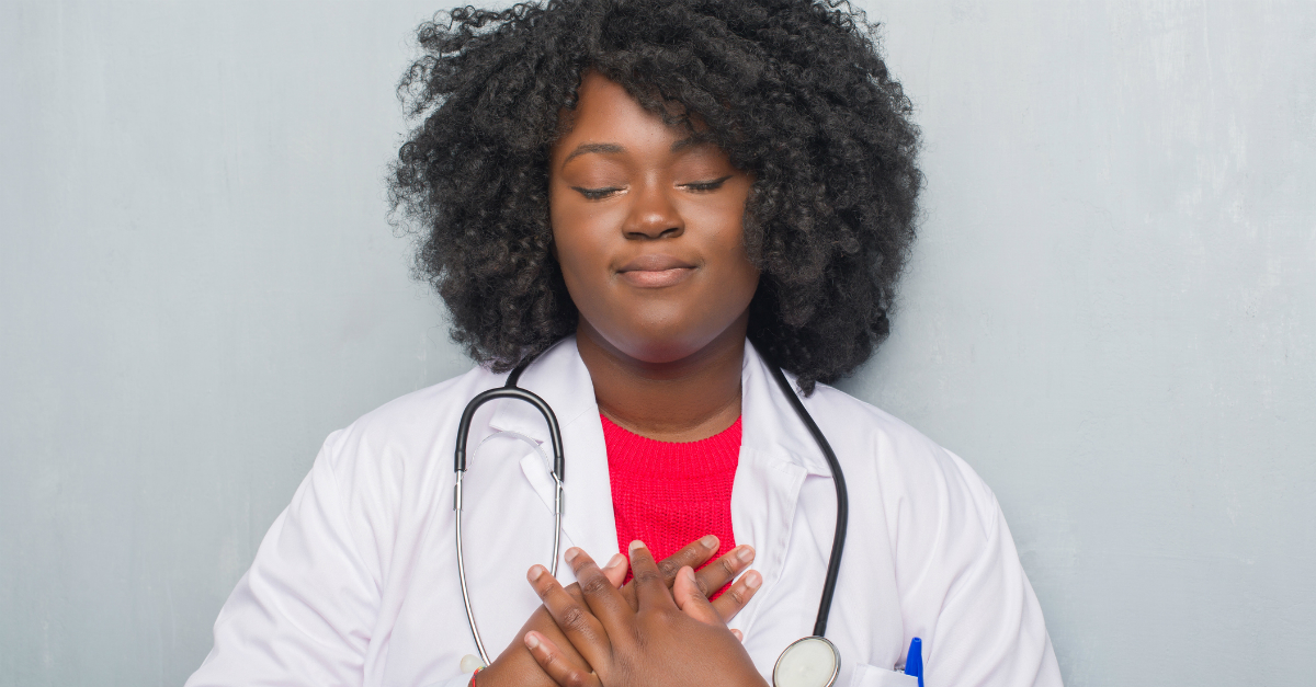 woman in doctor coat with stethoscope eyes closed hands over heart praying