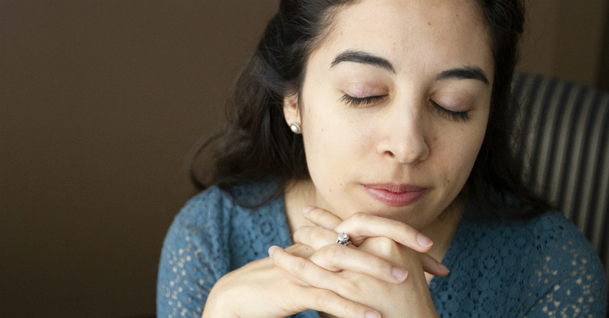 woman clasping hands in prayer under chin eyes closed