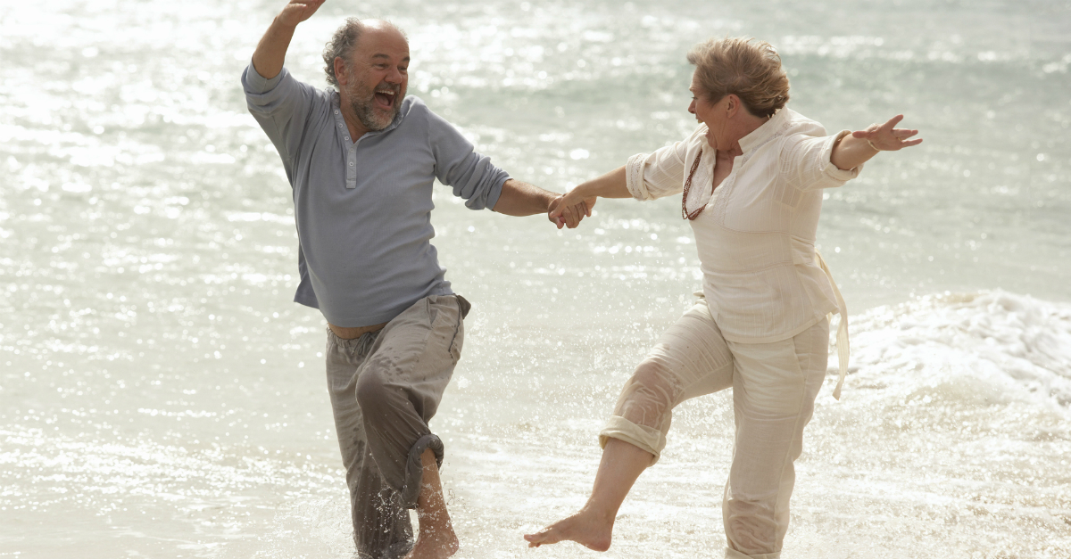 happy senior retired couple splash and laugh at beach