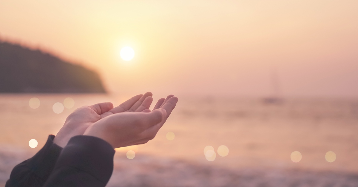 holding open hands up to soft light sunset