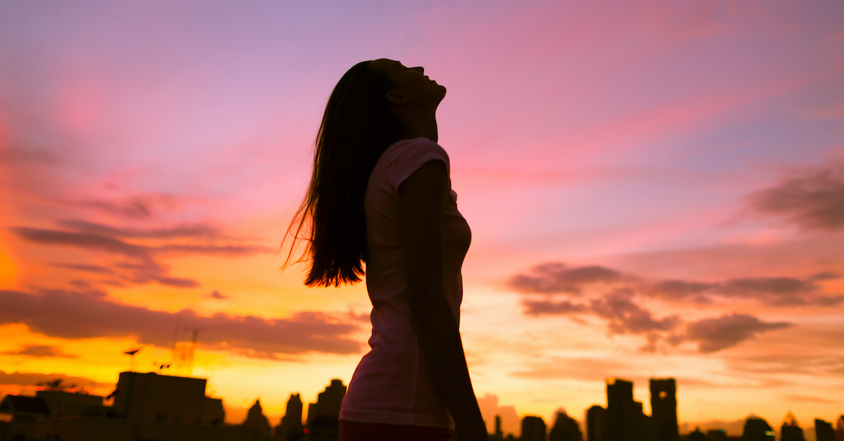 silhouette of woman looking up at sky during sunset against city scape