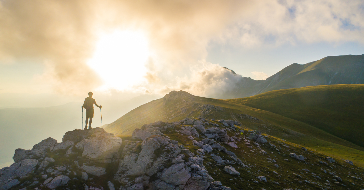 back view of man climbing over mountain range at sunrise