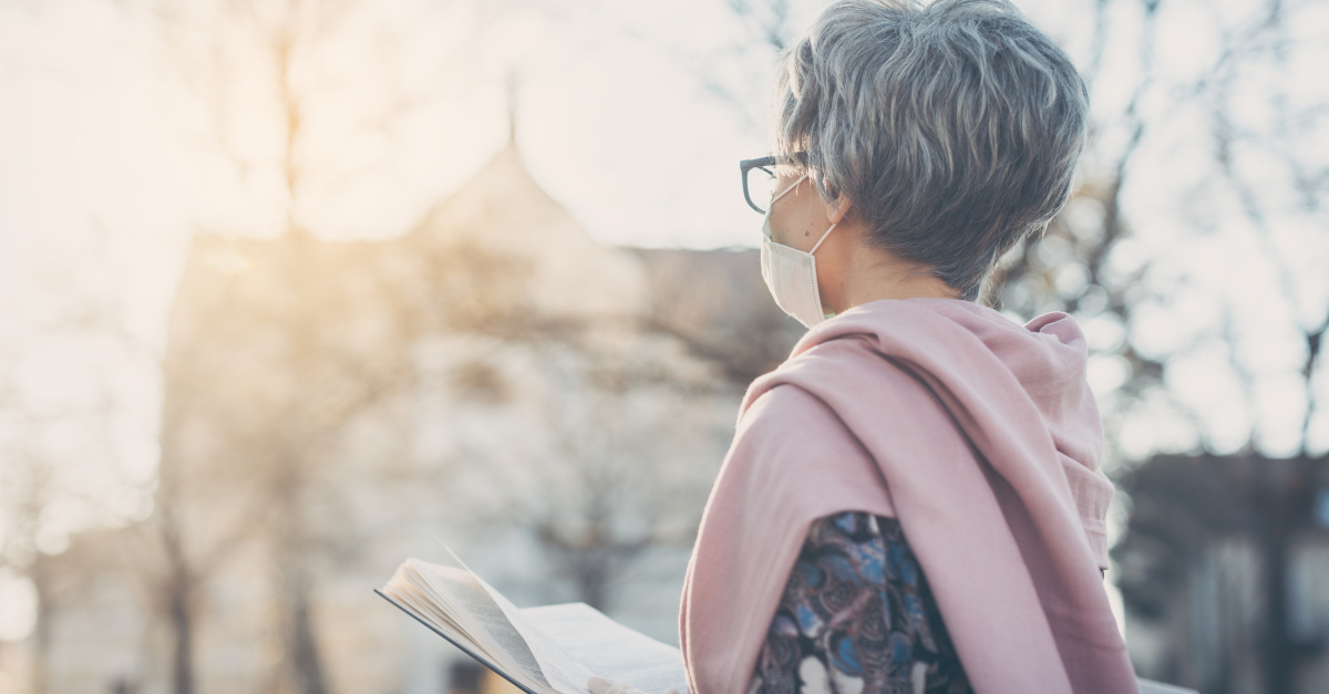 senior woman with face mask on during coronavirus with open Bible praying for church