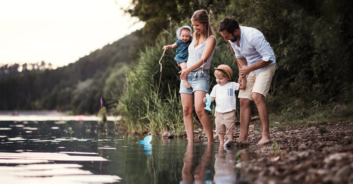 young family with little children playing with toy fishing poles by side of water