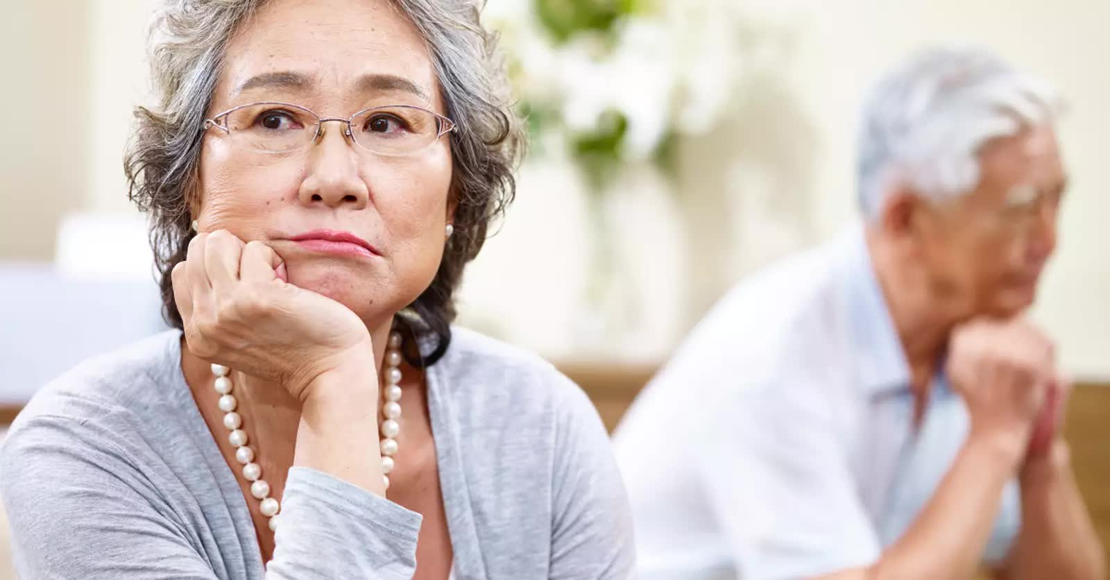 Elderly woman looking frustrated with her husband in the background