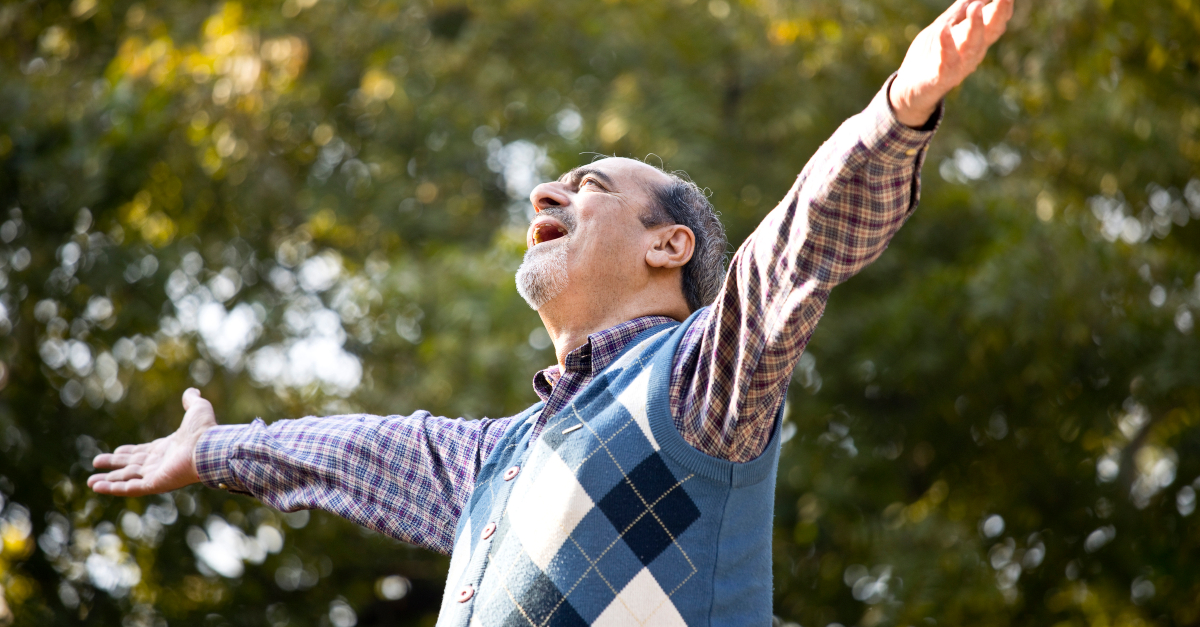 senior man arms wide looking up in praise