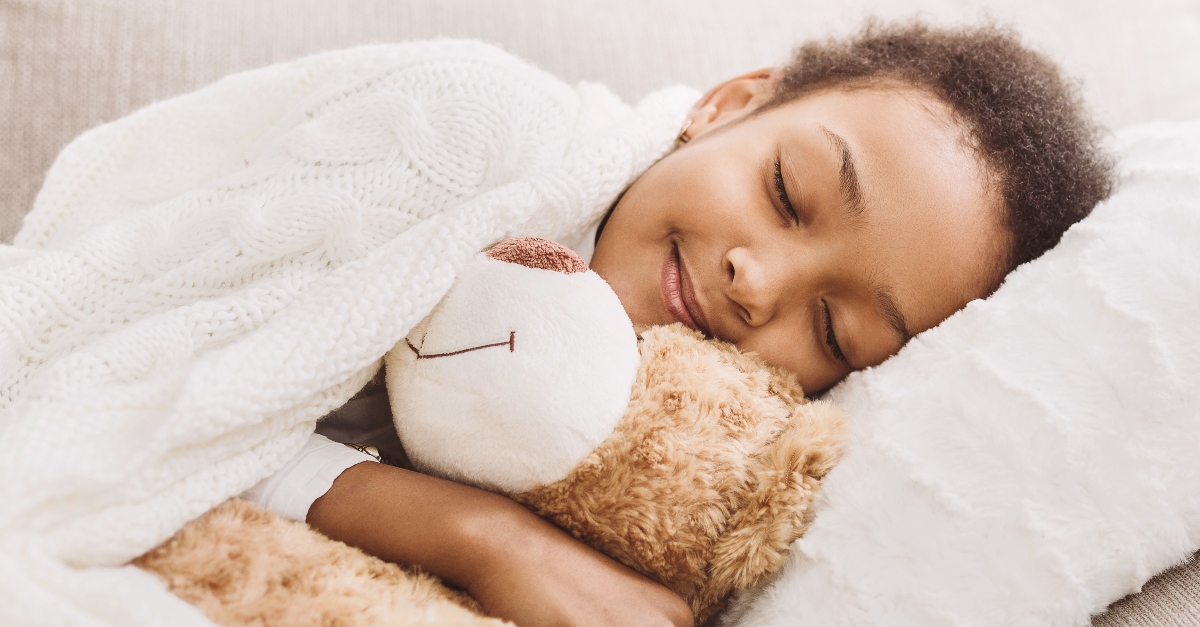 little girl sleeping peacefully in bed with smile on her face hugging a teddy bear, now I lay me down to sleep