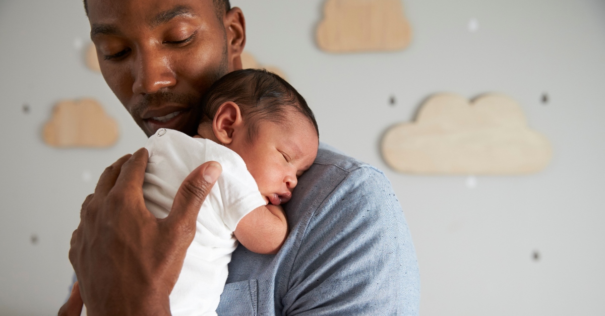 dad holding infant baby asleep on his shoulder