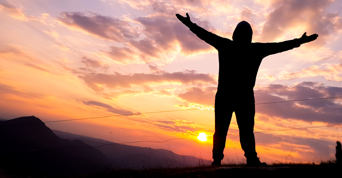 back view of adult arms out at sunrise in praise and worship