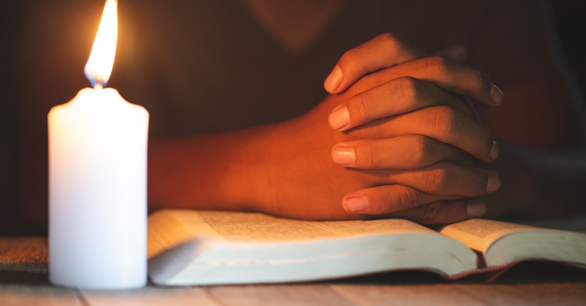 hands together praying over bible with lit candle, christians prayer closet