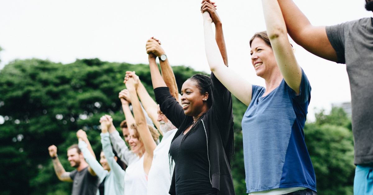 line of diverse people standing together holding raised hands