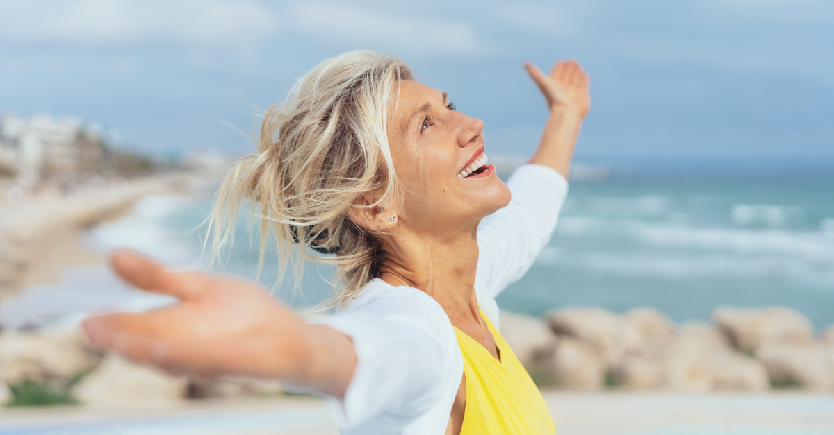 senior woman arms out wide on beach in joyful praise