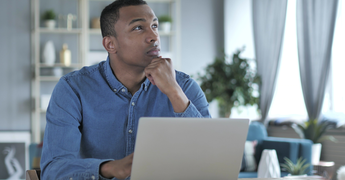 man looking up and off to right in deep thought at laptop