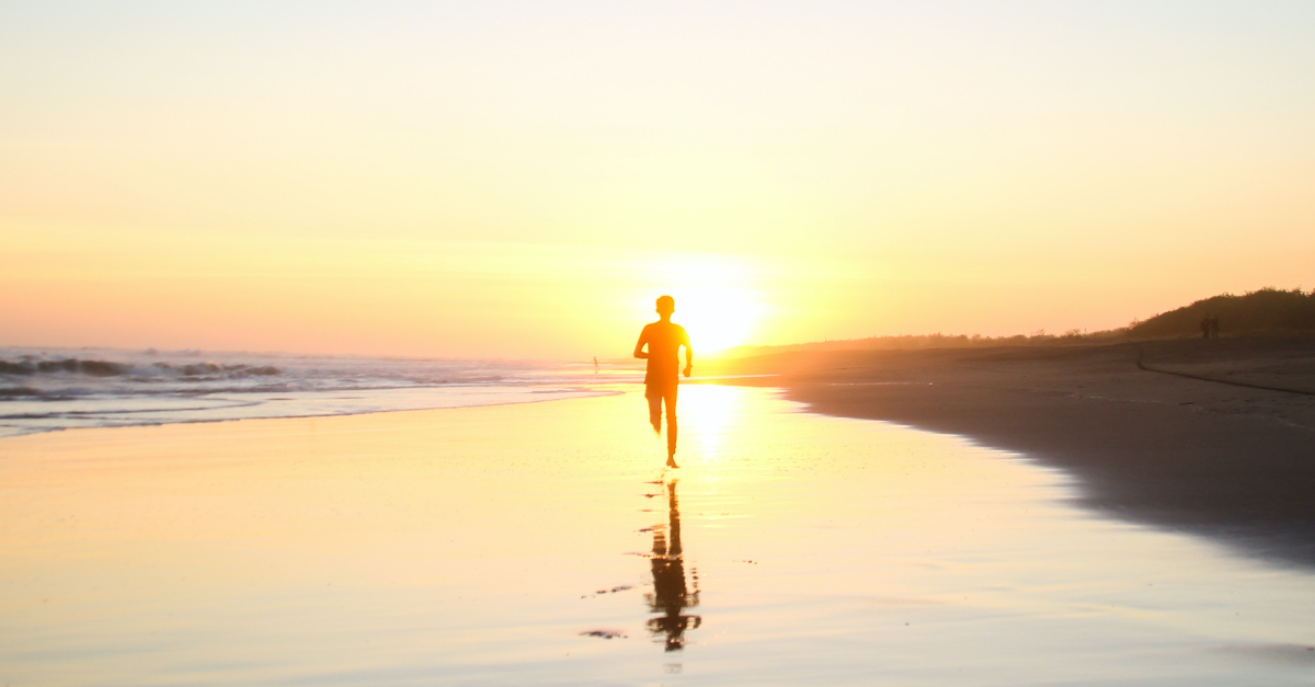 boy running down beach toward sunset at dusk