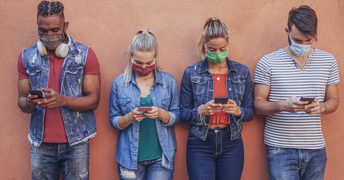teenagers with masks standing against wall using smart phones