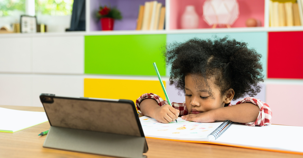 young child doing school on tablet while drawing