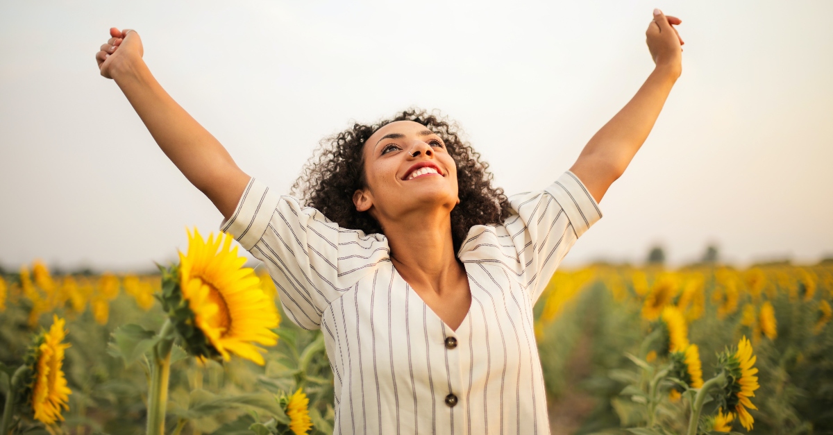 happy and joyful woman with arms in the air in a sunflower field, prayers of joyful defiance in tired world