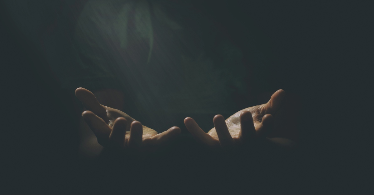 Hands outstretched in prayer in a dark background