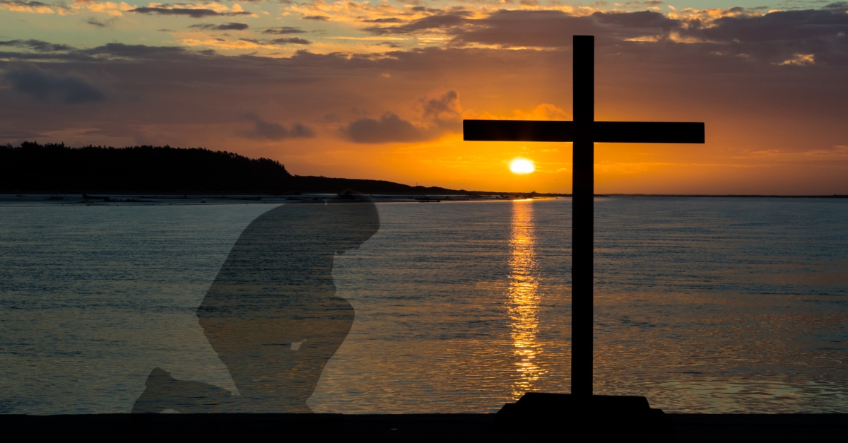 transparent image of man kneeling before the cross at sunset on water