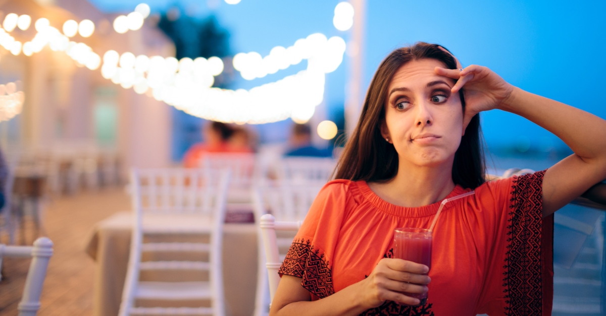 woman drinking alcohol at outdoor restaurant alone and bored