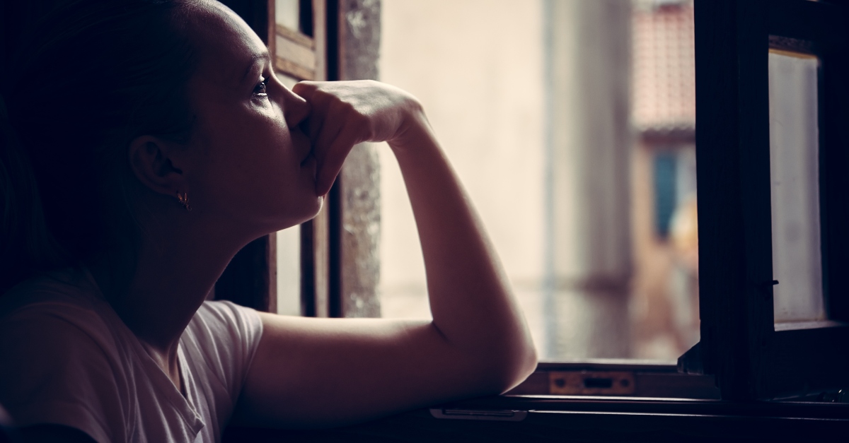 young woman looking out window thoughtful