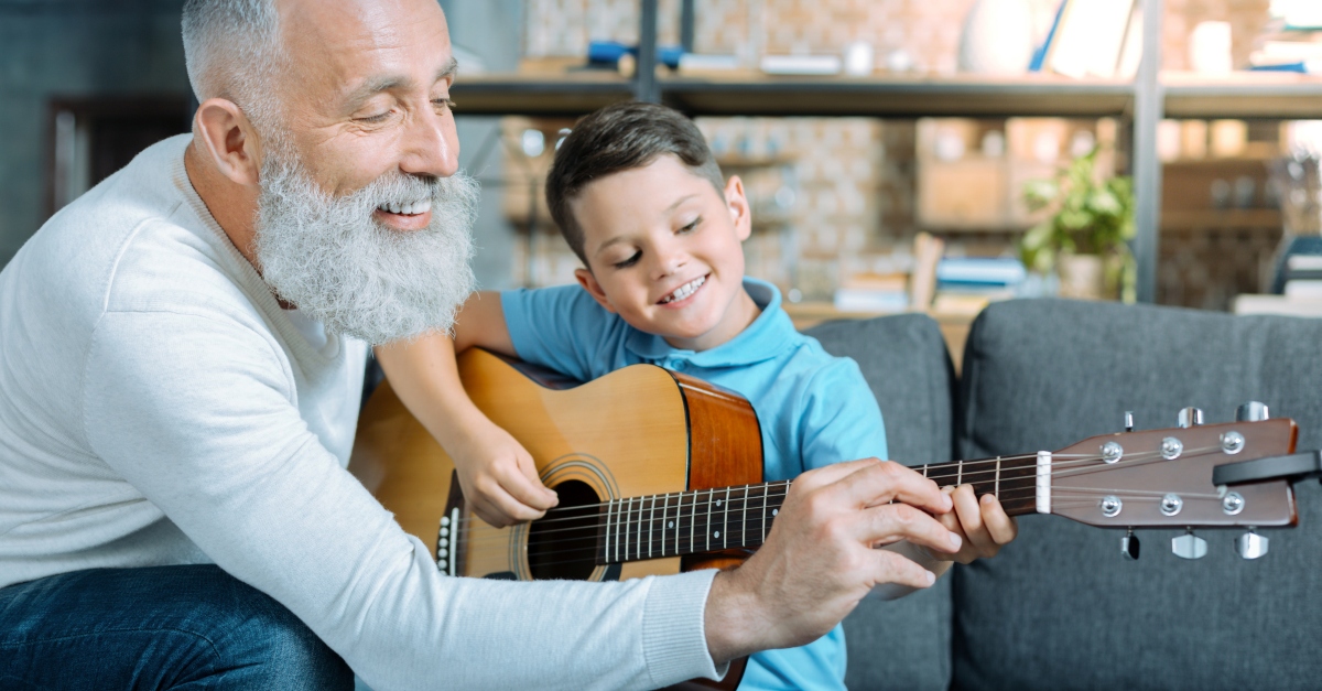 senior man teaching young boy how to play guitar in retirement