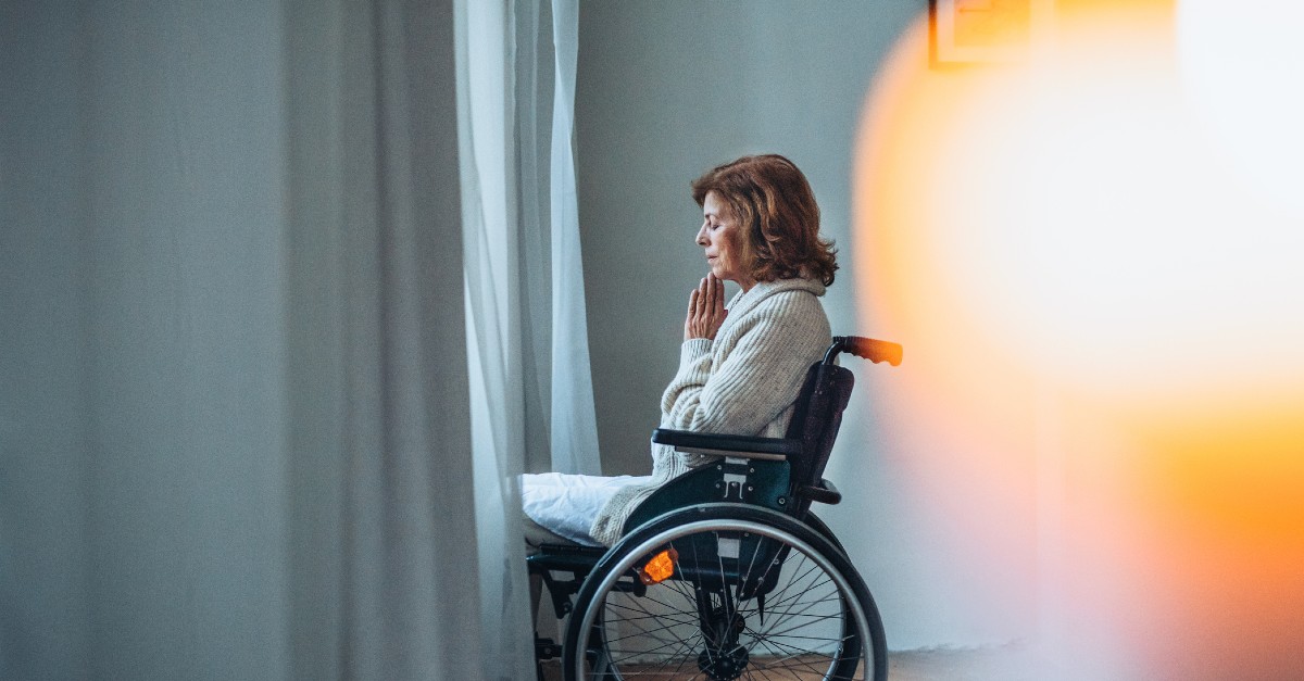 A woman seated in a wheelchair prays fervently before a window
