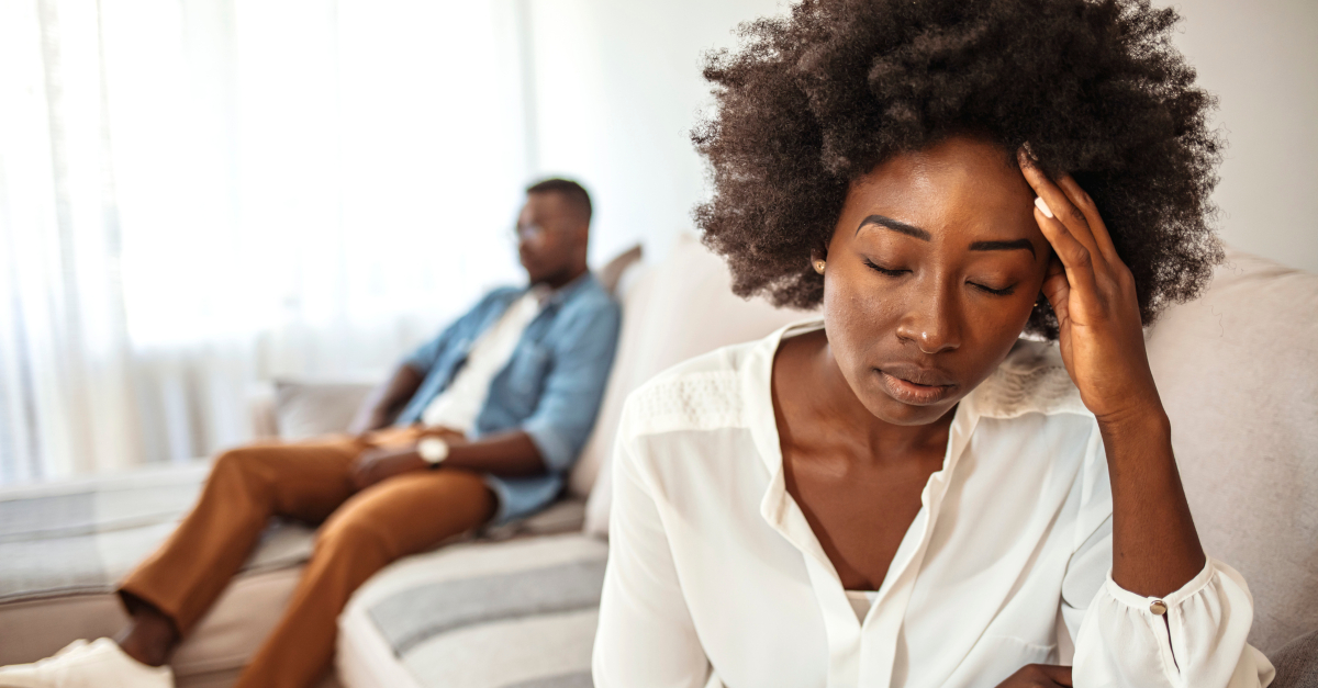 Close-up of an unhappy woman with her husband ignoring her in the background