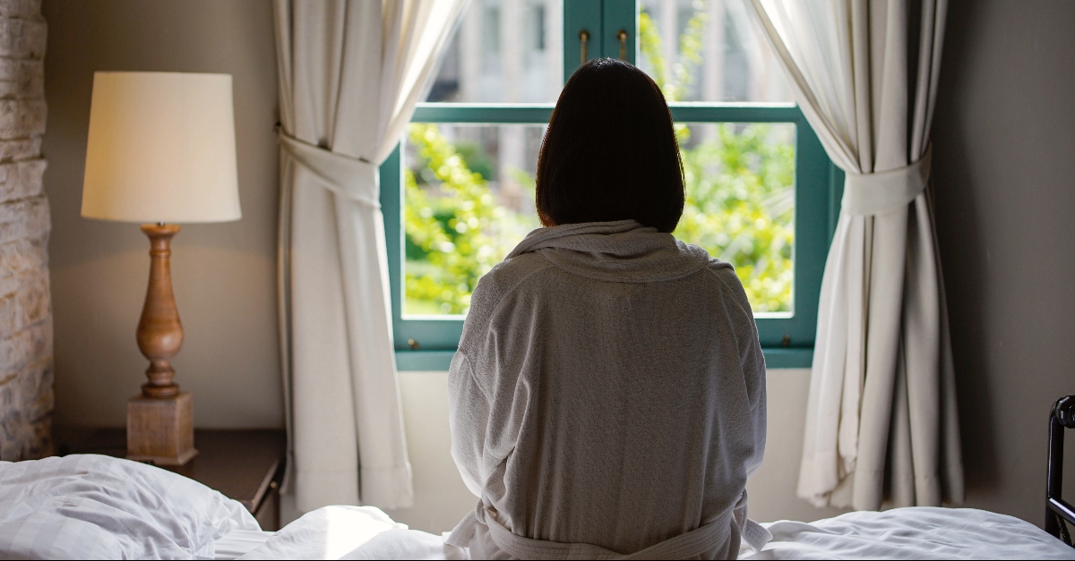 A woman sitting on her bed looking out her window