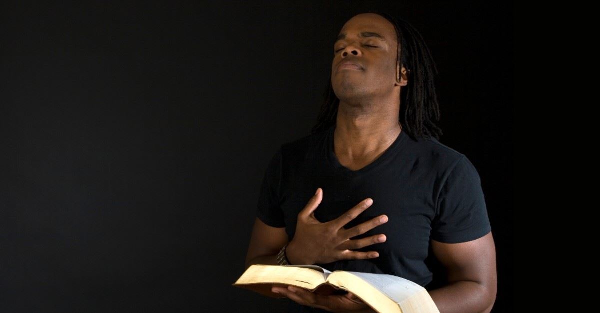 man holding Bible open with hand over heart in stance of prayer