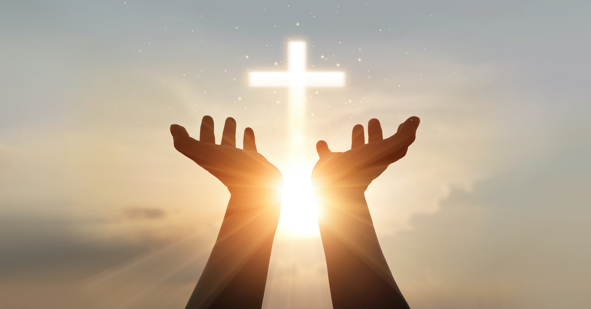 silhouette of raised hands toward cross graphic in bright sky