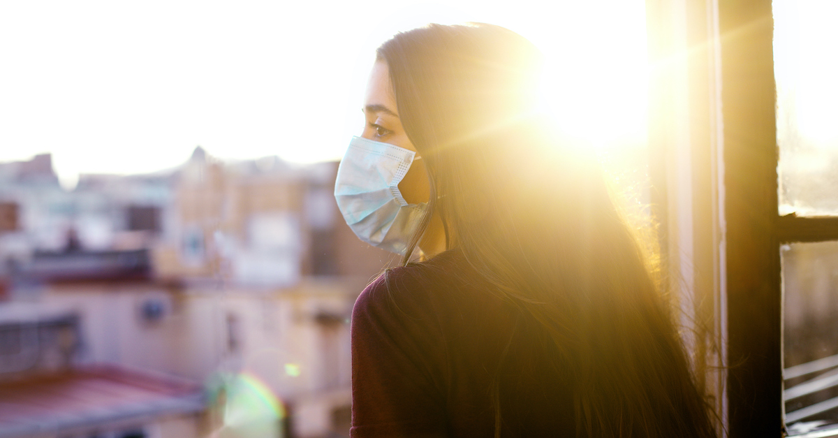 Woman wearing mask looking over balcony at sunset