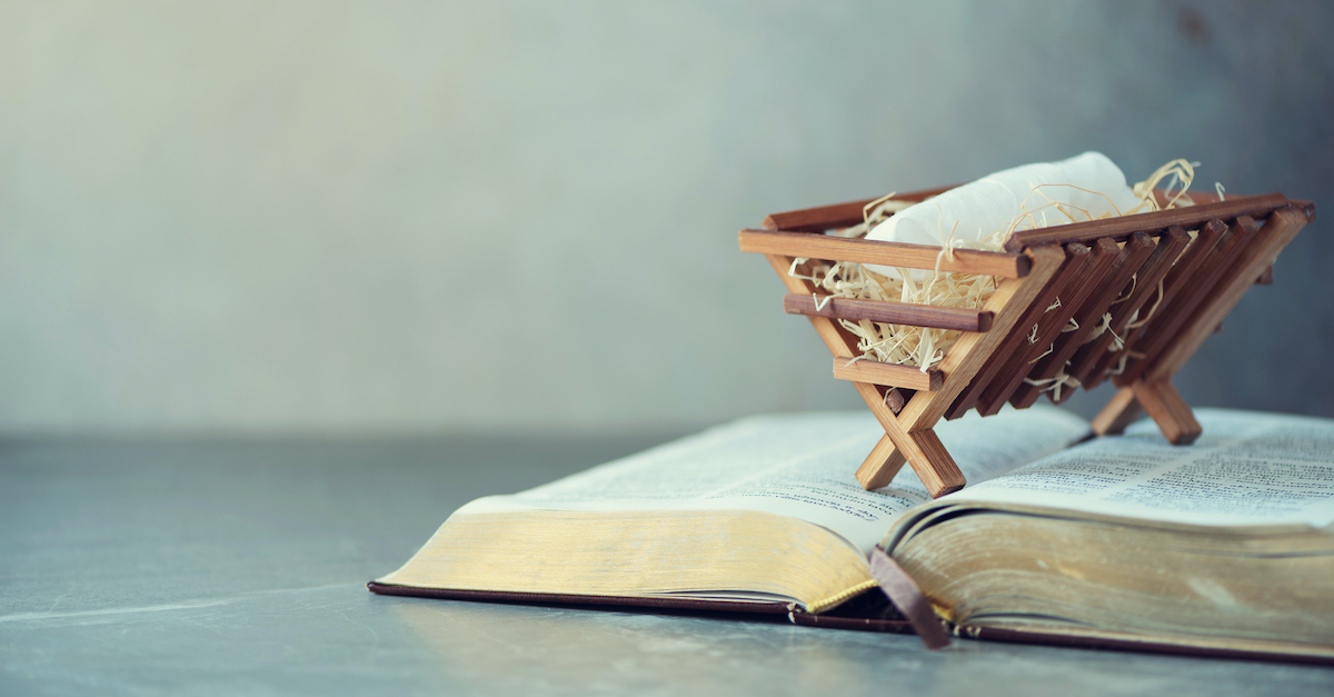 Small wooden nativity manger sitting on top of open Bible