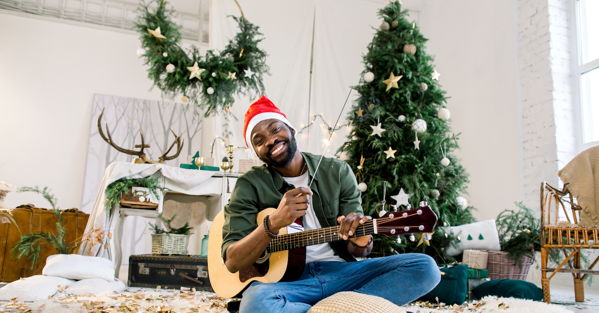 man wearing santa hat and holding guitar in Christmas decorated room with Christmas tree