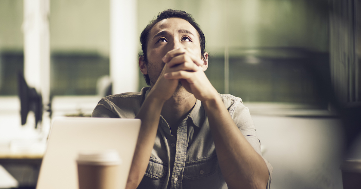 man looking upward with prayer hands at desk, God hears our prayers