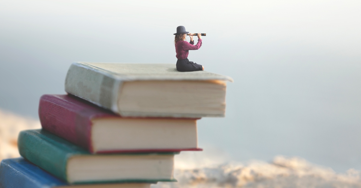 Woman looking out with a spy glass sitting on a pile of books